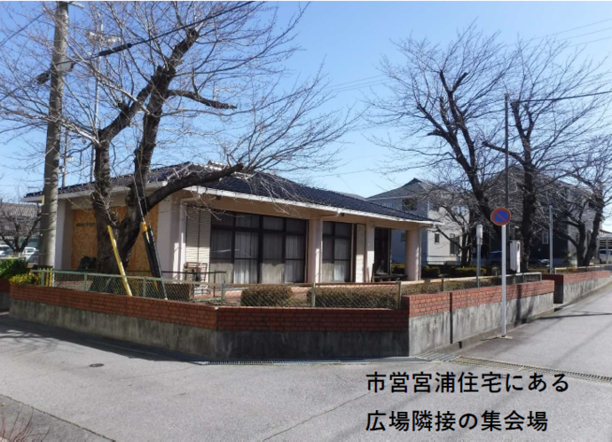 ⻄尾市営宮浦住宅 集会所の全体写真（平屋の建物の周囲に桜の木が並ぶ）