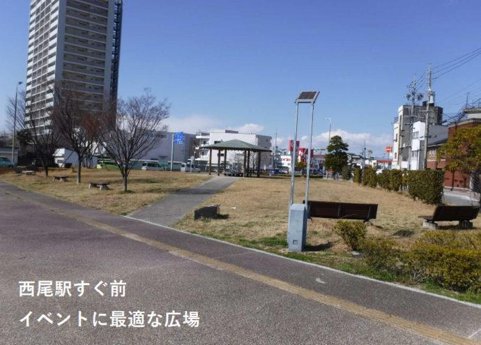 ⻄尾駅⻄多目的防災広場の全体写真（駅前にあるベンチなどが並んだ芝生の広場）