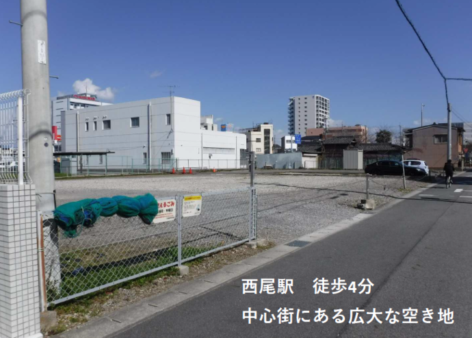 ⻄尾駅⻄再開発事業用地 ⻄側の全体写真（ビルや建物が周囲にある市街地に広がる広い空き地）
