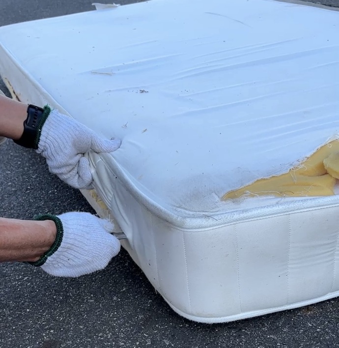 カッターでマットレスの側面中央を切り開く写真です